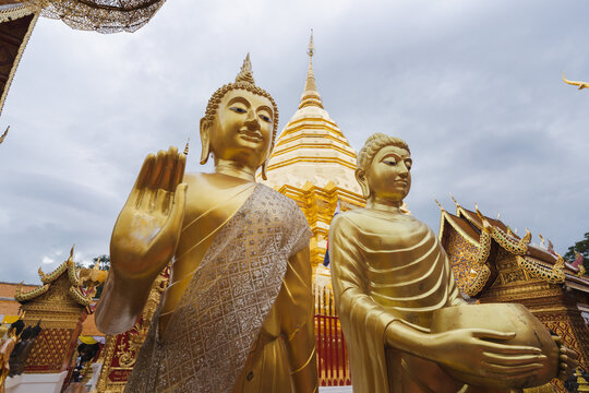 Golden Buddha statues in temple under cloudy sky in Thailand