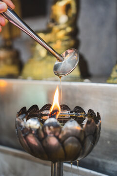 Anonymous Person adding oil into cup with burning candle in Buddhist temple in Thailand