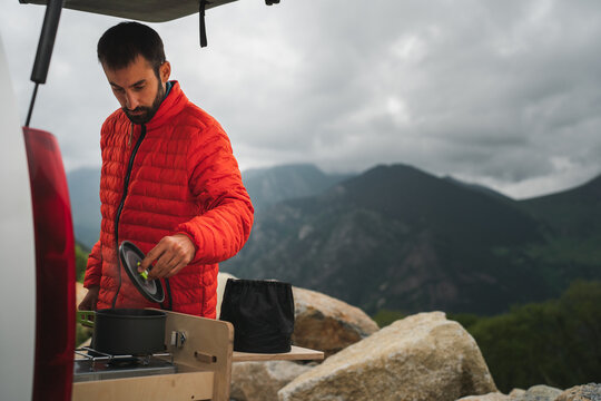 Man in winter jacker cooking food during hiking in countryside