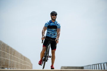 Sportsman standing on bike wearing helmet and sunglasses. Athletic male cyclist training with cycle...