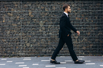 Business man in formal wear walking by the grey wall