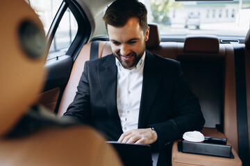 Business man sitting at the back seat of the car working on laptop