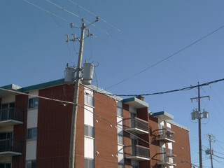 Immeuble d'appartements avec poteau électrique et fils contre ciel bleu clair. - 694843089