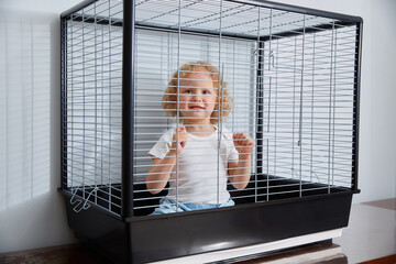 A cute smiling child is sitting in a large bird cage