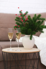 Two glasses of Champagne on caffee table in living room. Christmas home interior. Ceramic vase with fir branches.