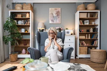 Fotobehang Senior woman sick and blowing nose at home from virus, allergy and illness on couch. Tired, tissue and elderly female person in a house lounge with sneeze from cold and flu on a sofa with allergies © Srdjan