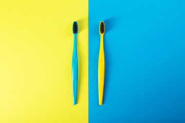 Yellow and blue toothbrush with charcoal coating on a yellow-blue background. The concept of dental and oral hygiene in dentistry. Copy space for text, medium hard. View from above. 