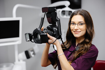 Portrait of female dentist holding photo camera in hands, standing in dental office