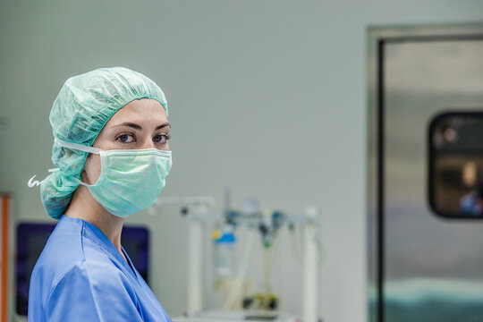 Female surgeon in uniform with medical mask and cap standing at hospital
