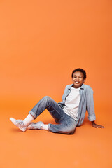 cheerful preadolescent african american boy sitting on floor and smiling happily at camera