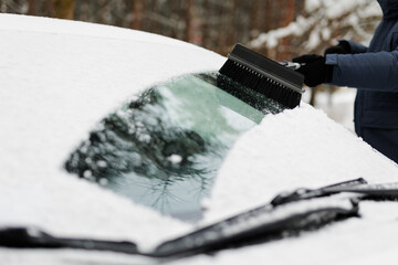 Man cleaning a snow covered car with brush