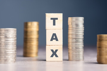 Tax word by wood cubes with different heights of money heaps, tax payment, tax planning