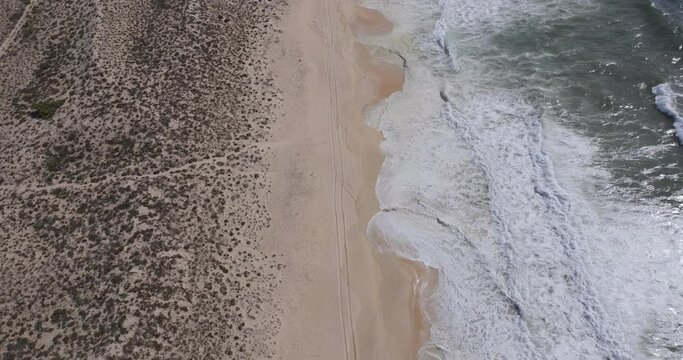 Aerial drone shot of sand dunes, beach, tyre tracks and shoreline with ocean waves breaking on beach near Comporta, Alentejo Coast, Portugal, Europe. Shot in 5k, ProRes 422HQ, exported in ProRes