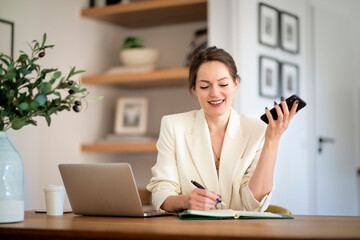 Confident woman sitting at home and using laptop and smartphone for work