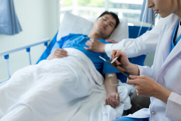 Obraz premium An Asian male patient lies in a hospital bed and is carefully looked after by a doctor. Doctor giving advice to male patient Working on health disease diagnosis