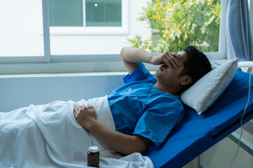 Young Asian patient on a hospital bed with a sad look at a hospital examining a patient on a bed while wearing a blue hospital gown.