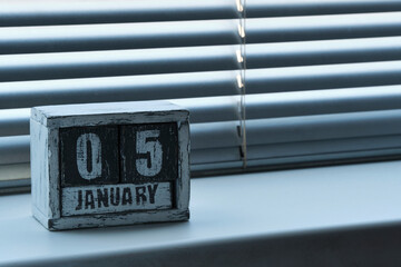 Morning January 05 on wooden calendar standing on window with blinds.