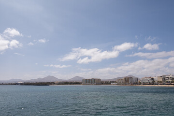 Fototapeta na wymiar View of the Reducto beach and mountains in the background, from the Fermina islet. Turquoise blue water. Sky with big white clouds. Seascape. Lanzarote, Canary Islands, Spain.