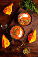 Pumpkin soup with seeds and spices in a dark bowl, herbs and sliced pumpkins on a wooden table,...