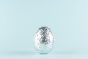 Easter egg wrapped in a silver foil against pastel blue background. Easter minimal concept....
