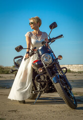 young woman in a bridal wedding dress and sunglasses on a motorcycle
