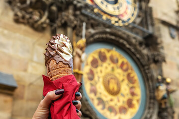 Female hand is holding traditional czech cookie trdelnik on background of Astronomical clock in Old...