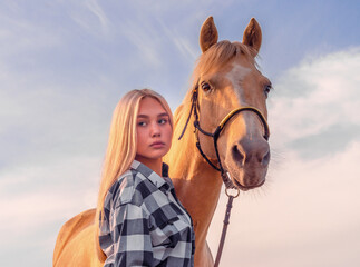 Obraz premium portrait of a young girl blonde with a beige horse against a blue sky with white clouds