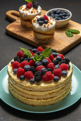 Homemade cake with fresh berries and sweet desserts on dark background.