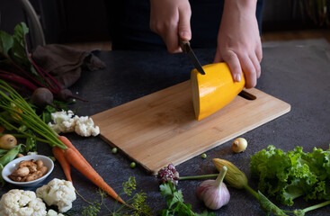 Close up of young woman hands cutting zucchini on wooden cutting board at home. Young woman preparing healthy food.