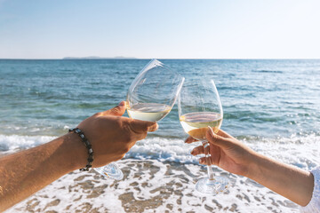 Two hands with glasses of wine on the beach. Summer vacations concept.