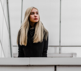 young girl with blond hair and black clothes against a gray building