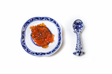 Red salmon caviar. Red fish roe on a white spoon with a blue pattern. Raw seafood. Elite delicacies. Protein healthy food. White background.  