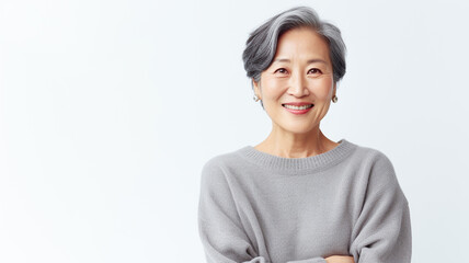 Portrait of a beautiful smiling senior asian woman standing with arms crossed over white background.