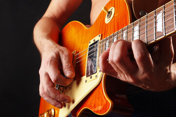 Hands of guitarist playing the orange guitar on dark stage.