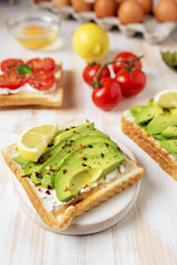 Sliced avocado on toast bread with spices on white wooden background. Food concept.