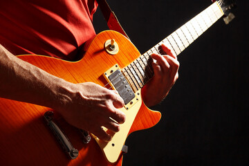 Rock musician in red plays the orange electric guitar on dark stage.