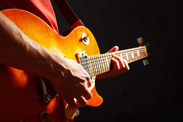 Musician in red with orange electric guitar on dark stage.