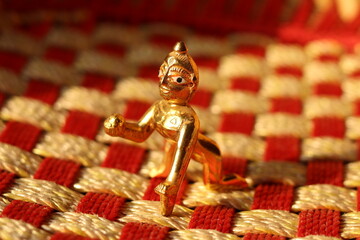 A shiny brass figurine of laddu Gopal or lord Krishna on a Check fabric pattern with background blur