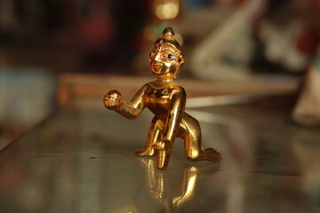A shiny brass figurine of laddu Gopal or lord Krishna on a glass surface with background blur,...