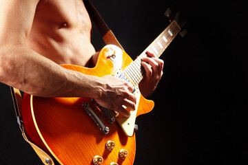 Rock musician plays the orange electric guitar on dark stage.
