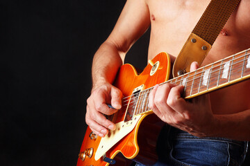 Guitarist with orange electric guitar on dark stage.