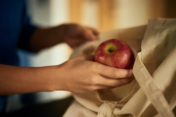Close-up of a female hand holding an apple, putting it in the cloth bag.