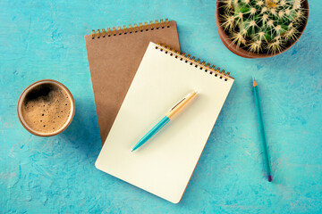 Notebook with a pen, coffee, and plant, overhead flat lay shot on a vibrant blue background, a mockup