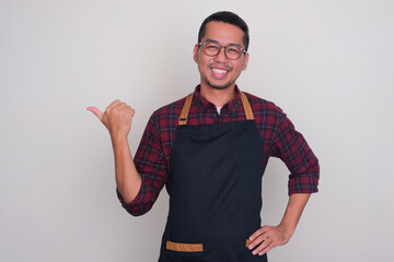 Asian man wearing apron smiling and pointing to the right side with his thumb