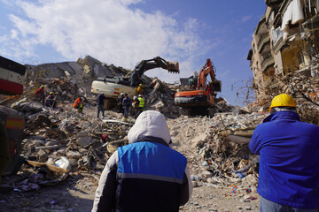 Rear view of a rescue team in jackets and hoodies in the middle of a large earthquake site...