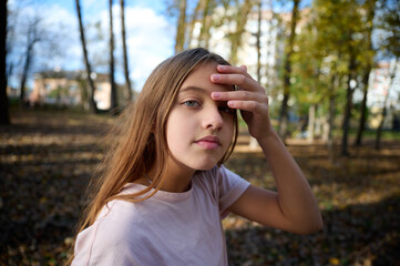 Naklejka premium Portrait of cute young girl in the autumn park in sunny bright day. Close up.
