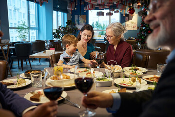 Happy senior woman sitting at table with little boy enjoying Thanksgiving dinner