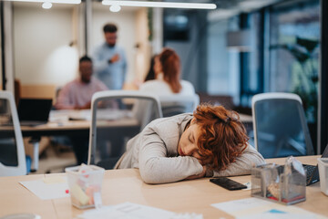 A tired businesswoman sleeping at her working desk in the office. She seems exhausted and...