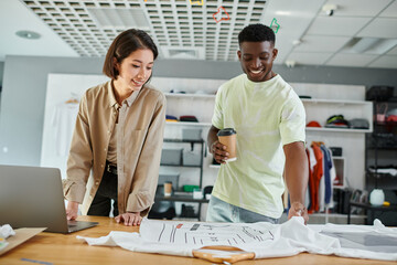 happy multiethnic fashion designers looking at clothing with format sizes in print studio, teamwork