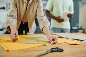 partial view of female fashion designer measuring sewing patterns in print studio, creative work